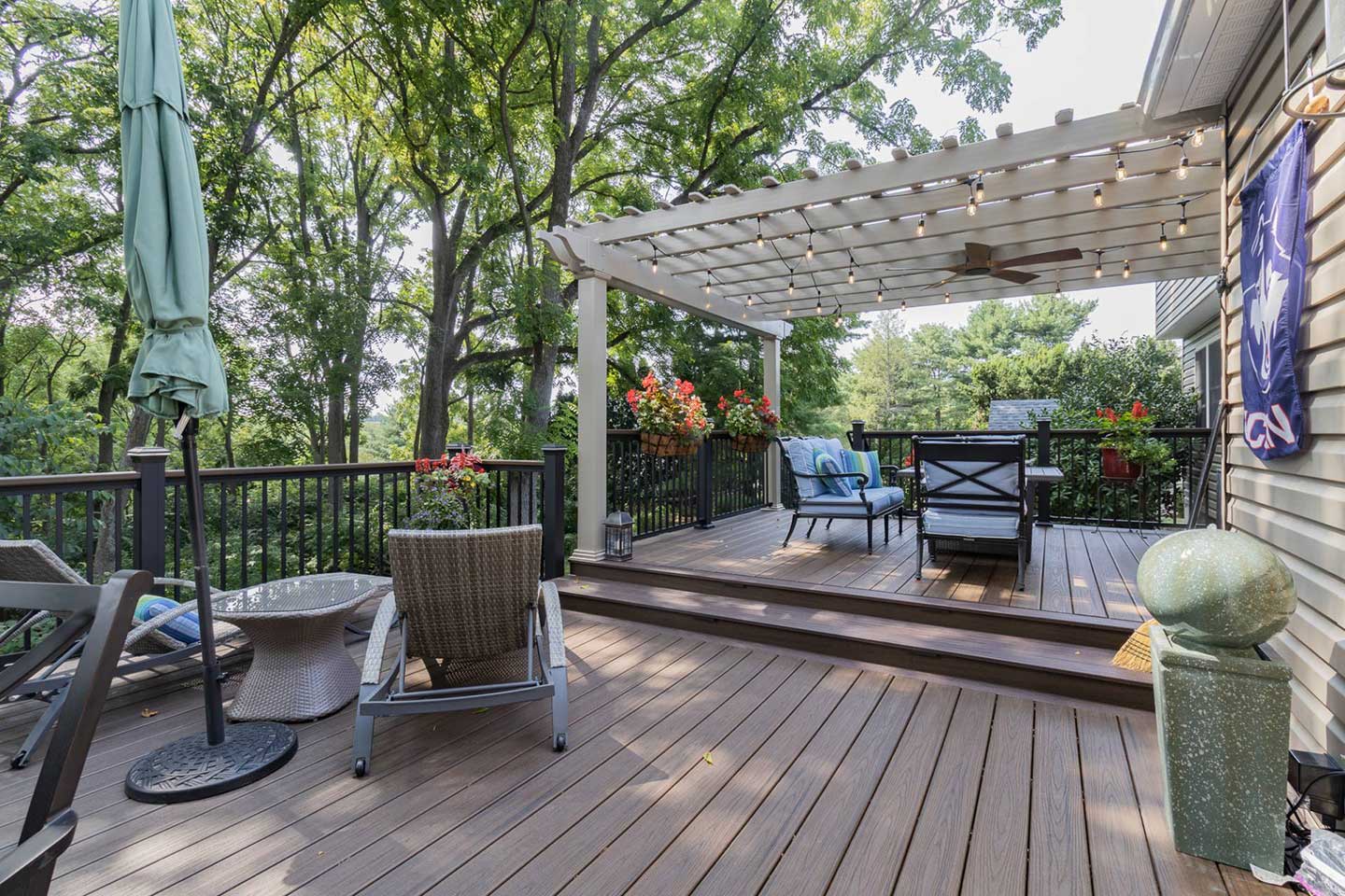 A second story luxury wood deck off the back of a house with a pergola overtop